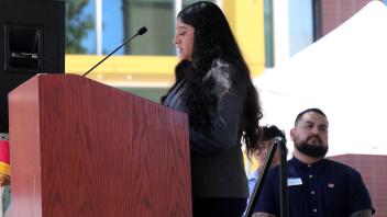 A young woman in a blazer speaks at the podium as previous speakers look on