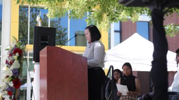 A young woman speaks at a podium while a fellow participant prepares behind her