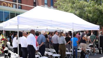 Attendees stand in respectful silence under white canopy tents during the UC Davis Memorial Day Ceremony 2025, held outside a campus building on a sunny day